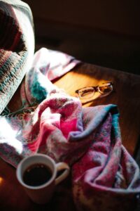 Reading glasses and a mug of a hot drink resting on a folded blanket