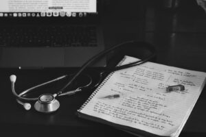Notebook and stethoscope beside a laptop, laid out as a nursing school supply kit