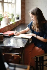 A student sitting at a desk writing in an open notebook beside a window