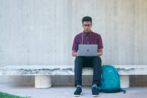 A student working on a laptop while sitting on a bench outdoors between classes